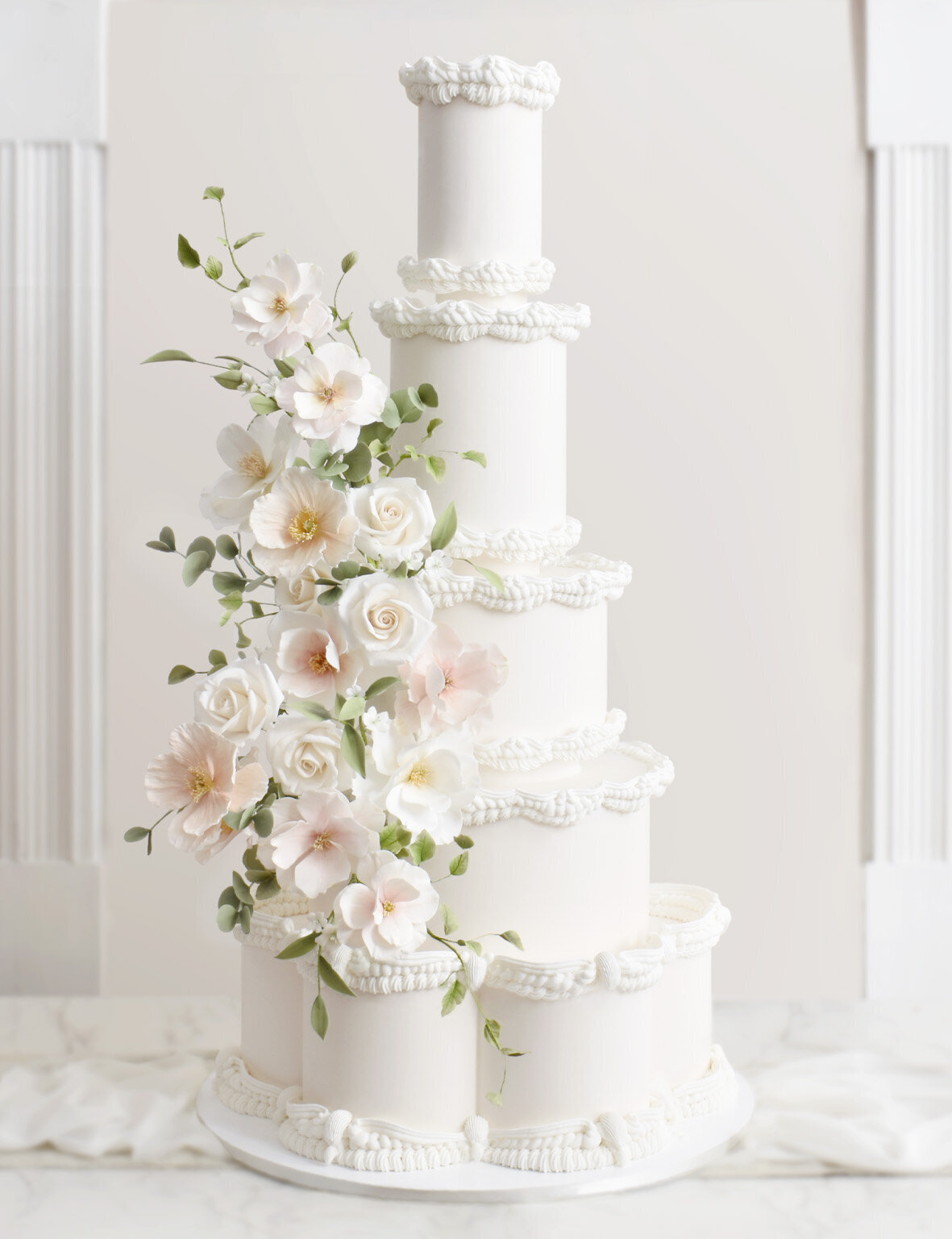 five tiered white wedding cake with elaborate piping and sugar flower cascade