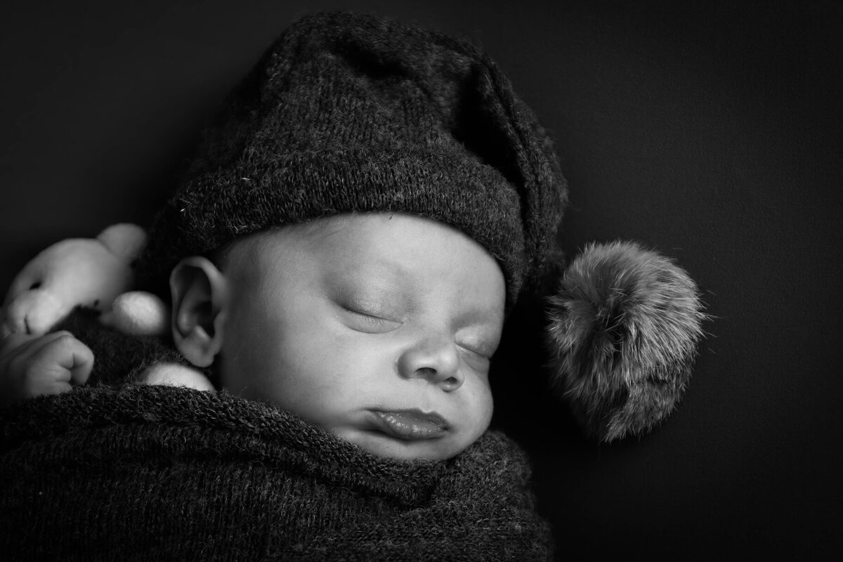 Black and white photo capturing newborn baby and his favorite teddy