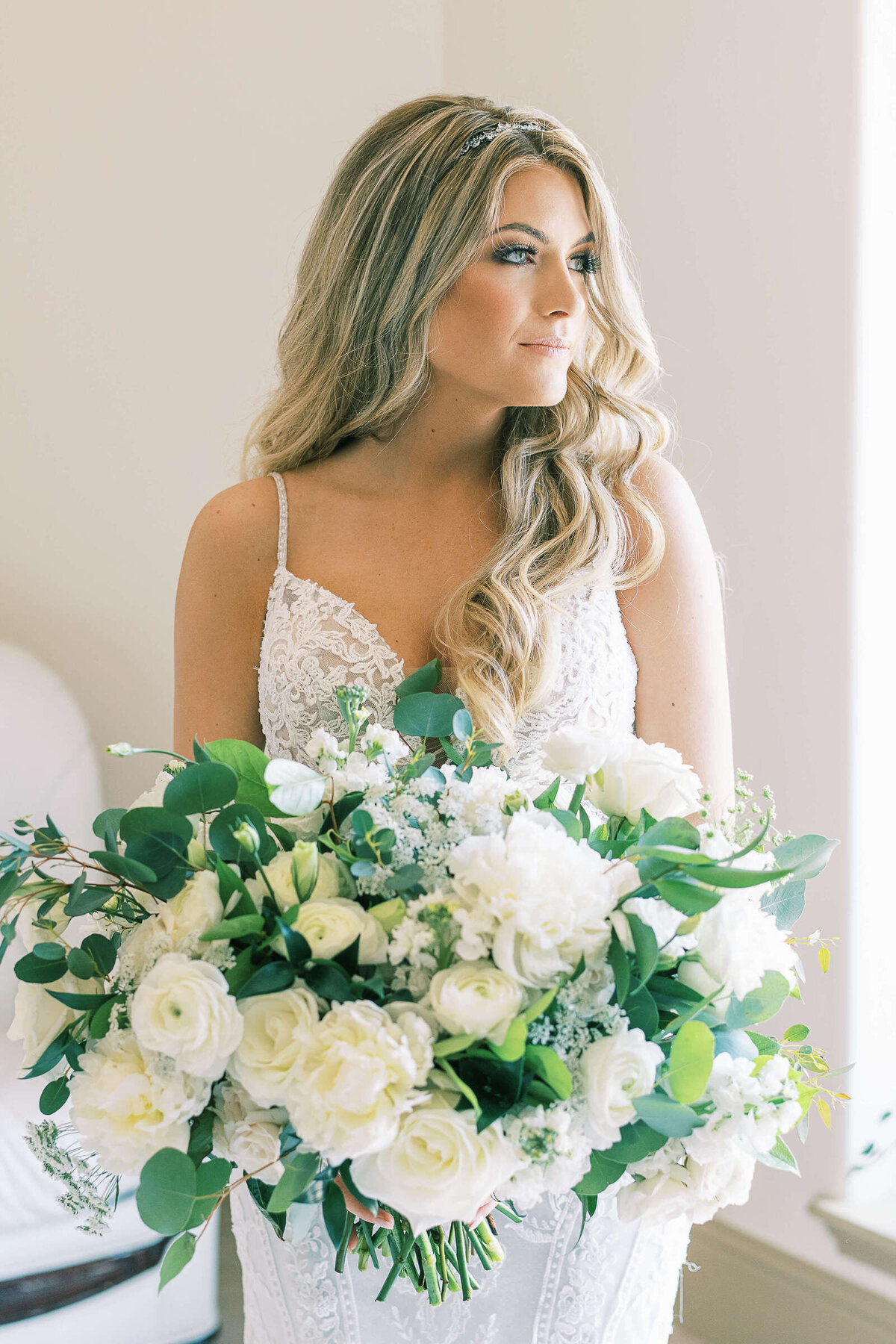 Elegant bride looks into the distance while holding large white wedding bouquet