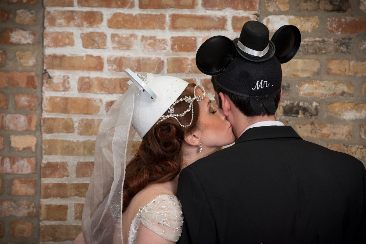 Bride kissing groom with wedding mickey mouse ear hats on