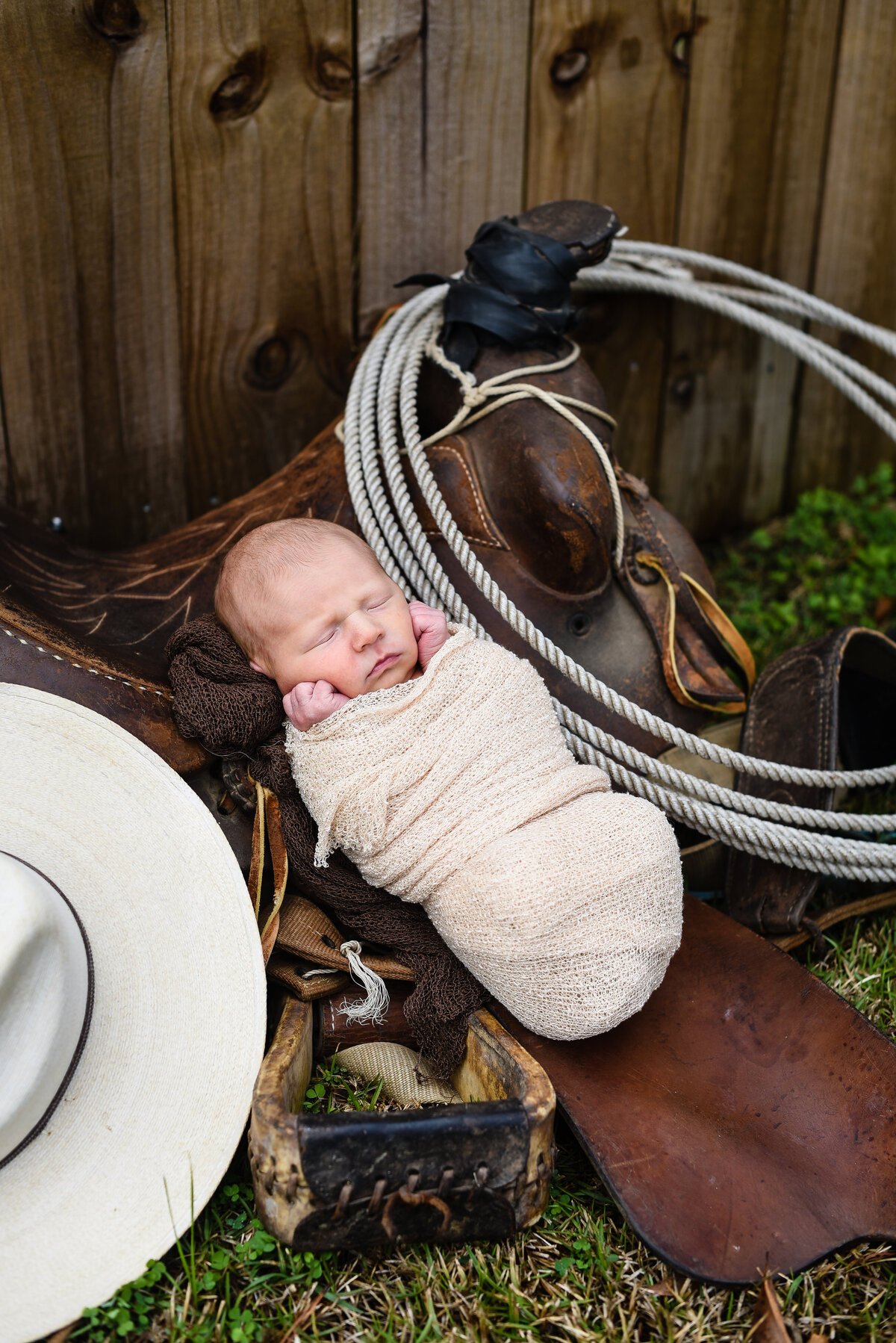 Beautiful lifestyle newborn photography: newborn boy lays in his dad's saddle with cowboy hat nearby in Mississippi