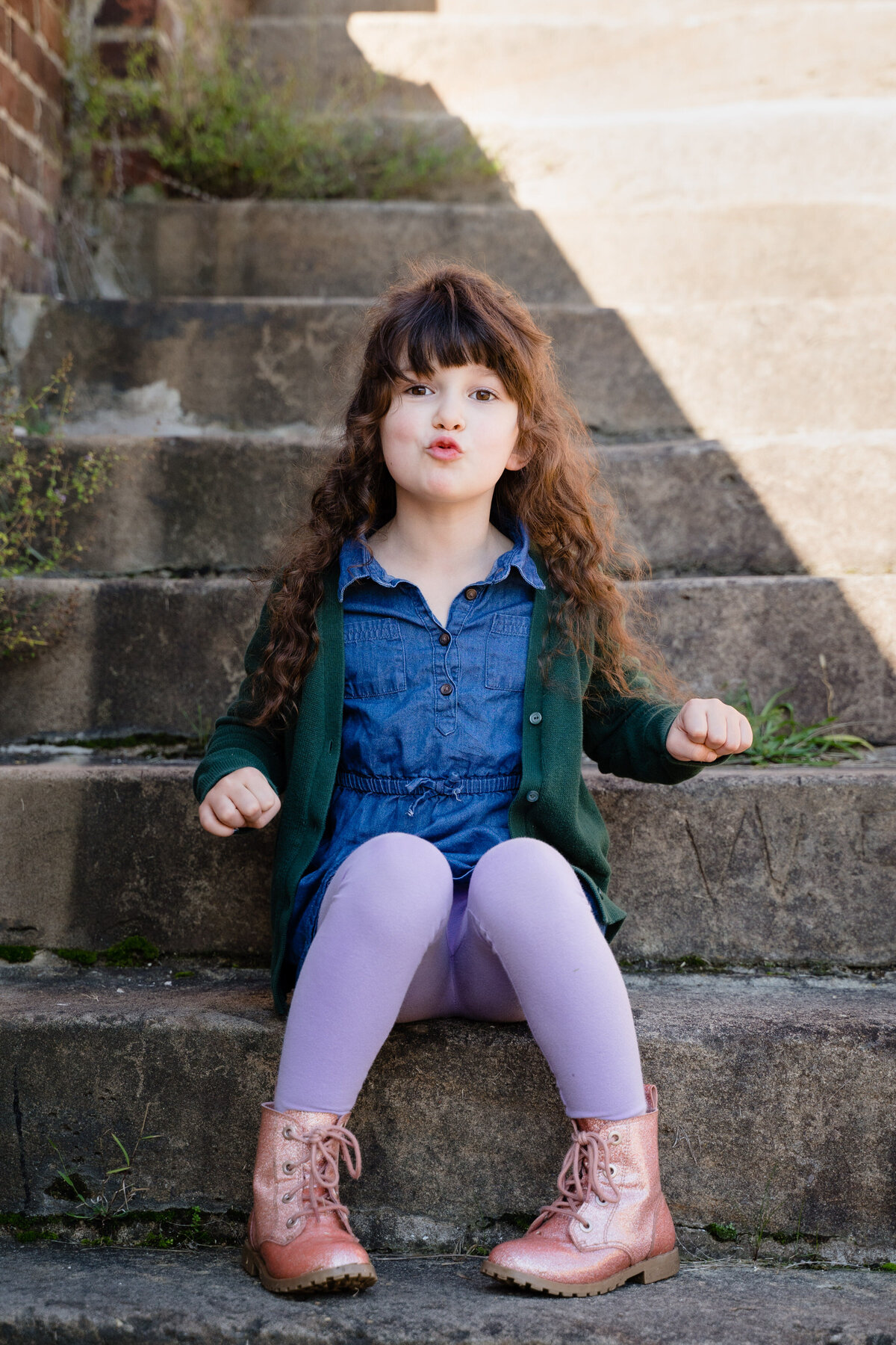 A small child sitting on stone steps making a funny face.