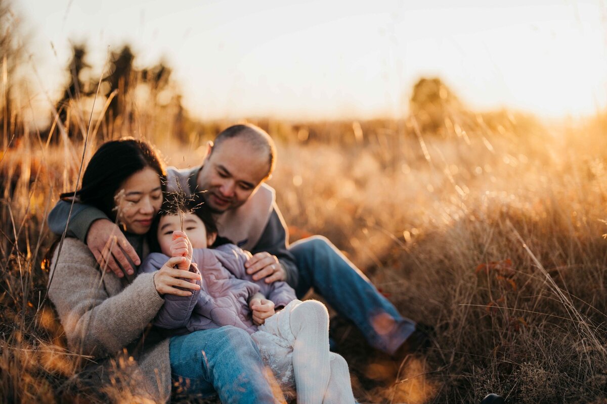 family-of-three-snuggling-at-sunset-in-meadow