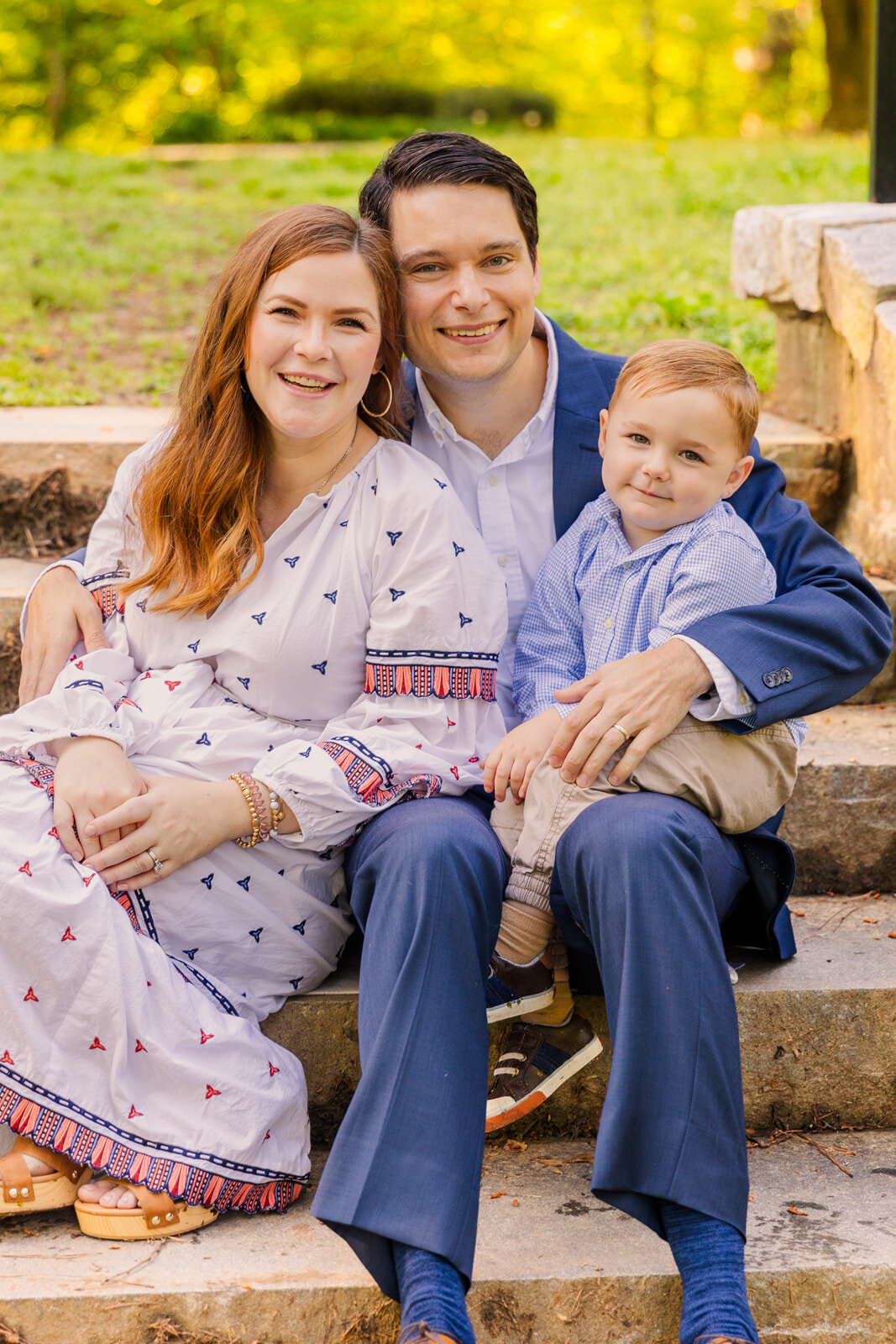 Parents with toddler boy sitting on stairs steps wearing coordinated white and blue outfits during photoshoo with Laure Photography