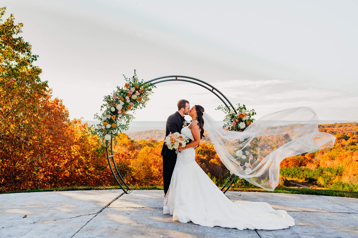 Photo of a bride and groom kissing in front of mountains with her veil blowing in the wind