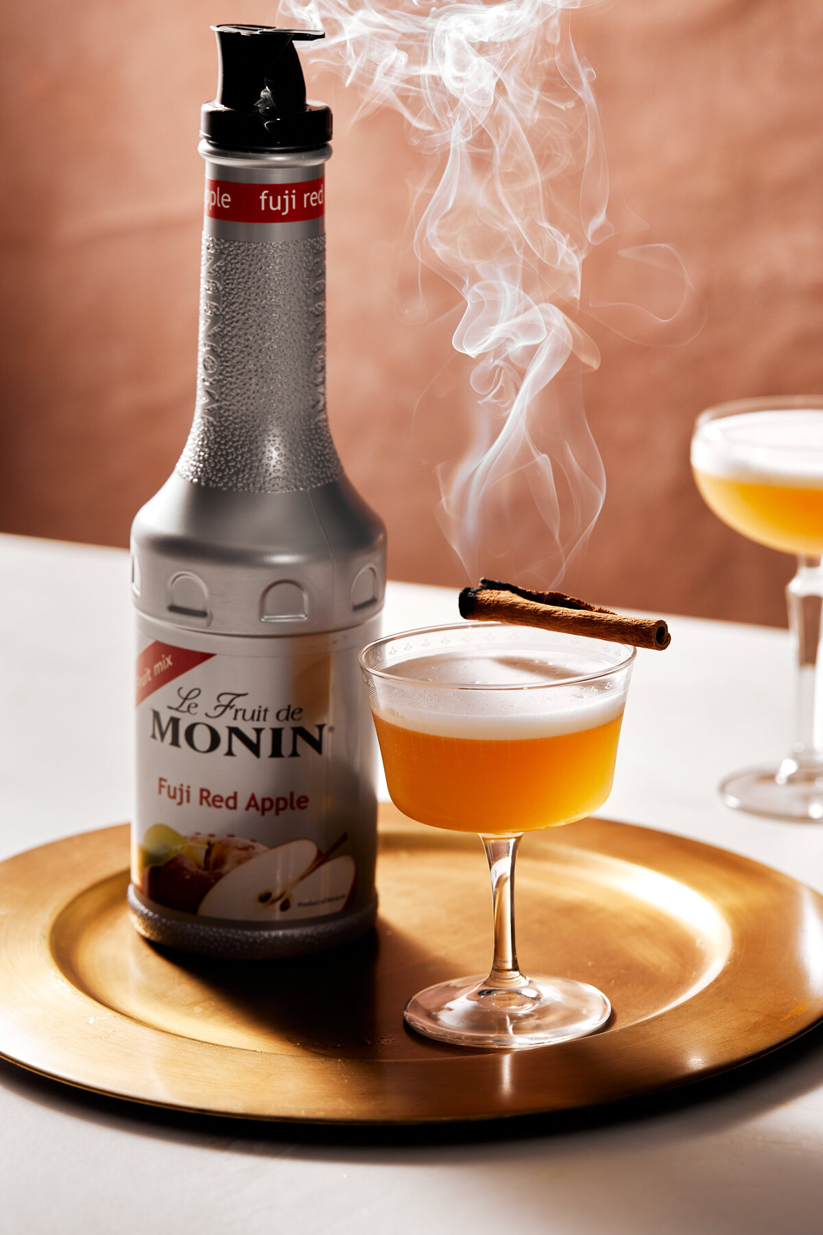Smoking cinnamon on top of a red apple cocktail drink.