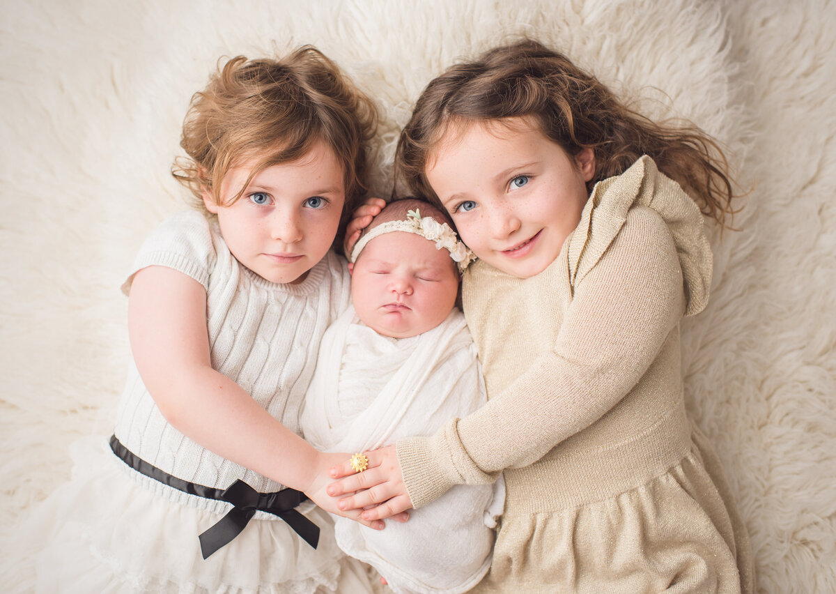 two sisters on either side of their baby newborn sister
