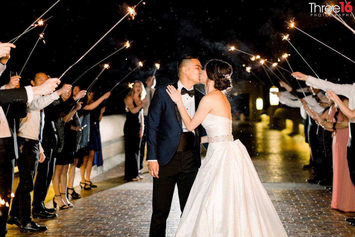 Bride and Groom kiss under a human tunnel of sparklers