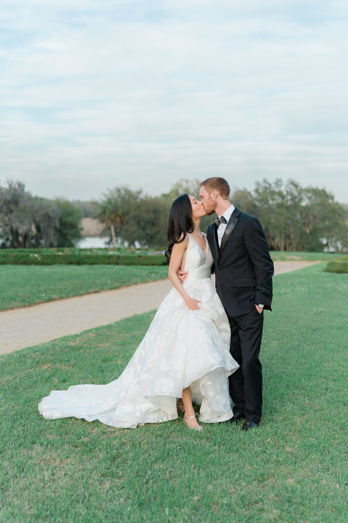 Sunset wedding day portraits. Winter wedding at Middleton Place. Bride and groom kiss on green grass with the last bits of sun warmly hitting them. Charleston destination wedding photographer.