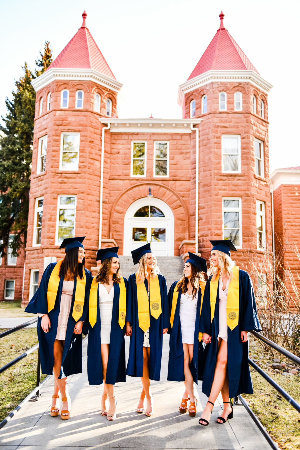 NAU Old Main senior friends group holding hands at Old Main in cap and gowns Northern Arizona University