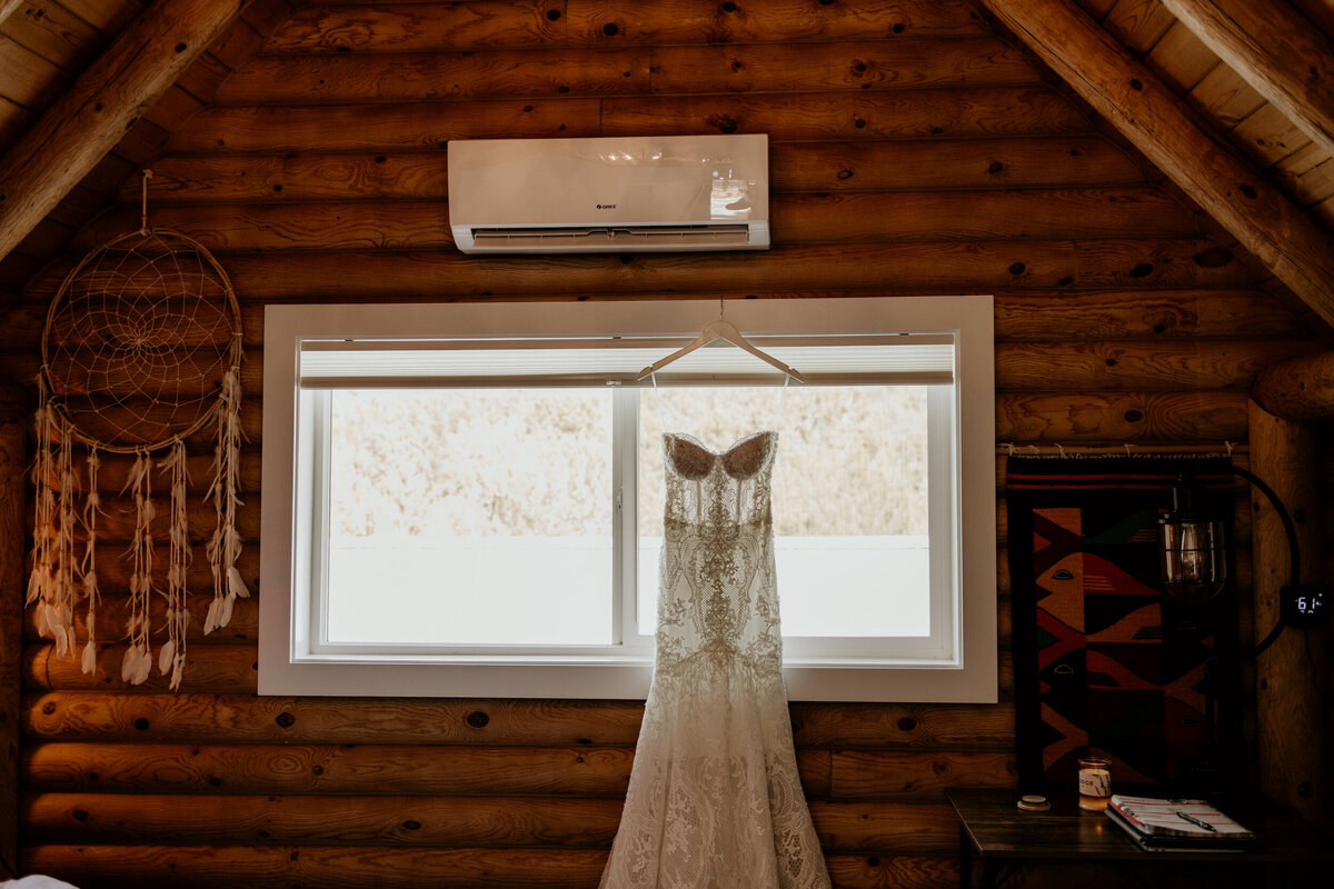 lace wedding dress hanging in front of a window