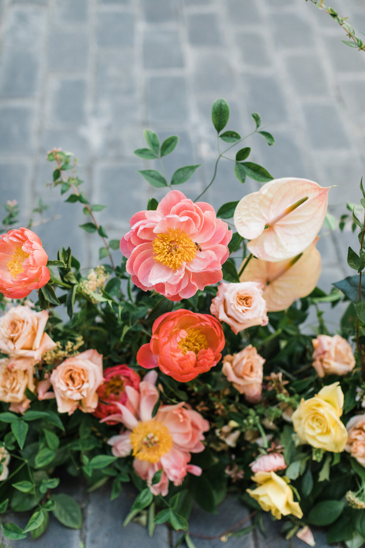 A detail shot of a floral arrangement for a wedding at the Hotel Crescent Court in Dallas, Texas. The floral arrangement is made up of many type of pink, orange, yellow, and red flowers and is resting on a brick floor.