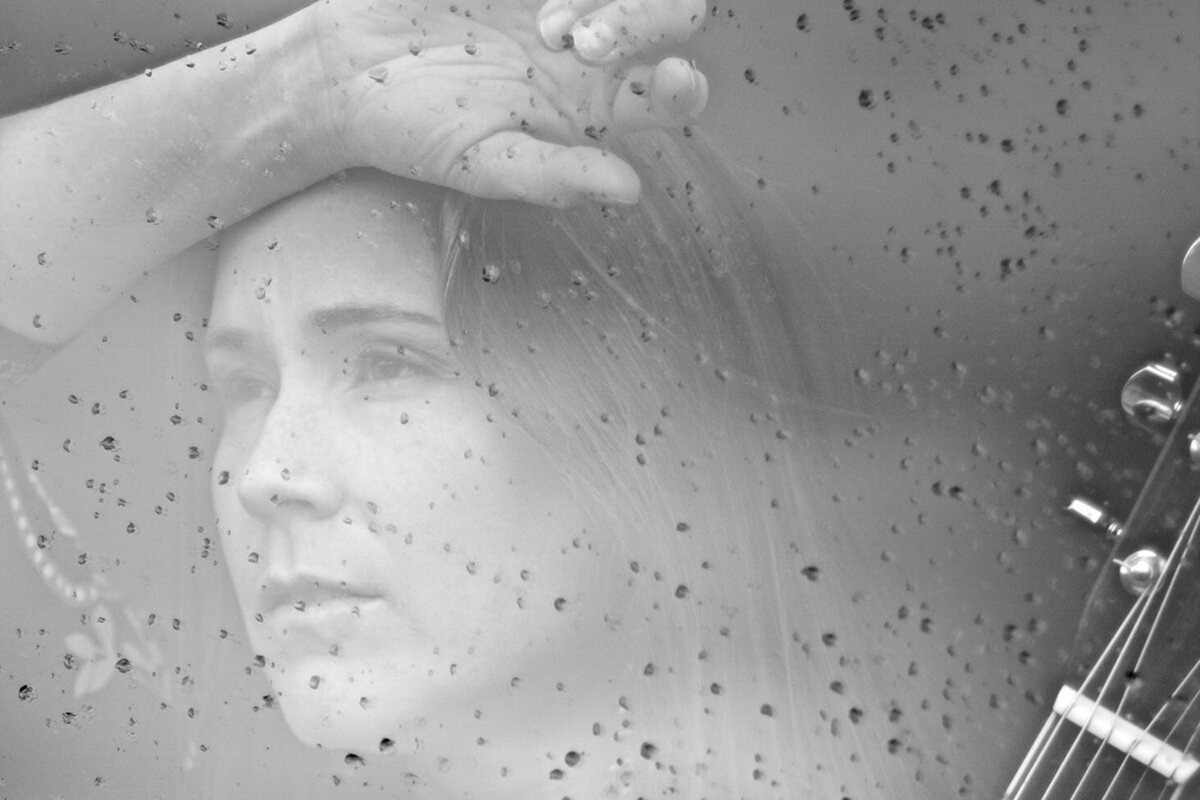 Female musician portrait Jessica Rhaye  black and white close up behind cloud reflections  on window with raindrops