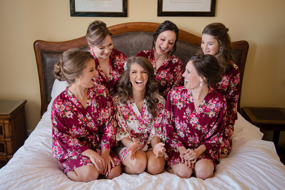 bride sitting on bed with bridesmaids all in floral silk robes