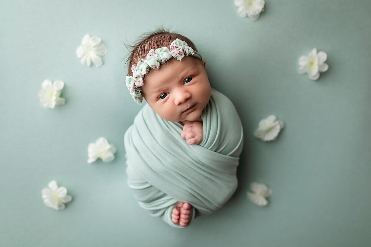 Wrapped newborn girl surrounded by flowers.