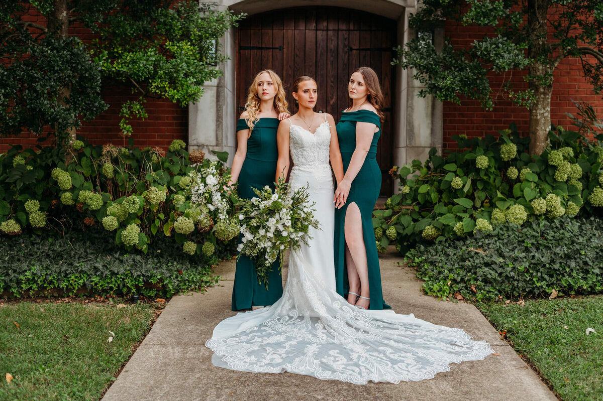photo of a bride standing with two bridesmaids and Emeril dresses while they stay or end of the distance in front of hydrangea bushes