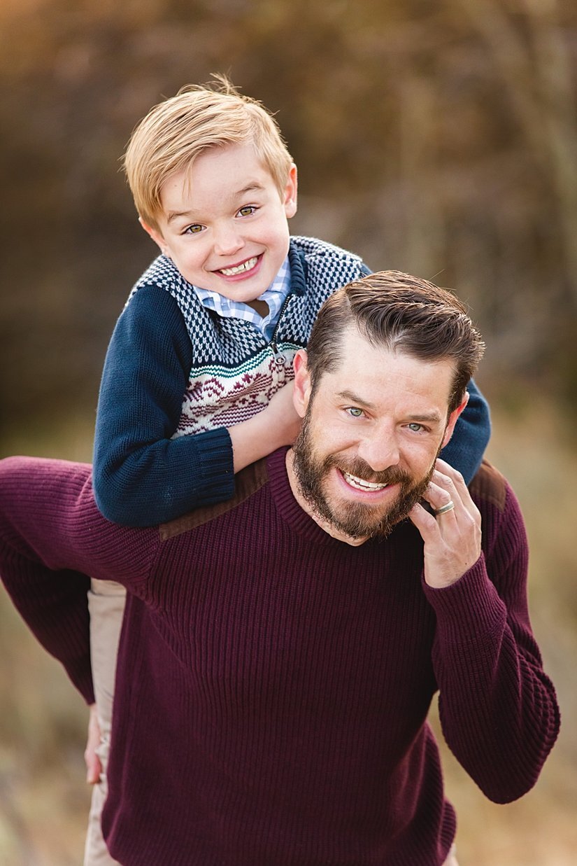 A father and son dressed in burgundy and blue with his cute little boy on his back.