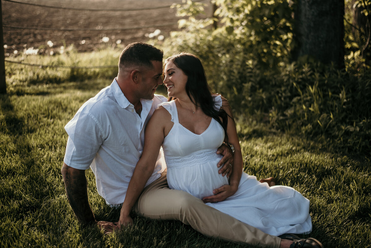 man and pregnant woman sit on grass