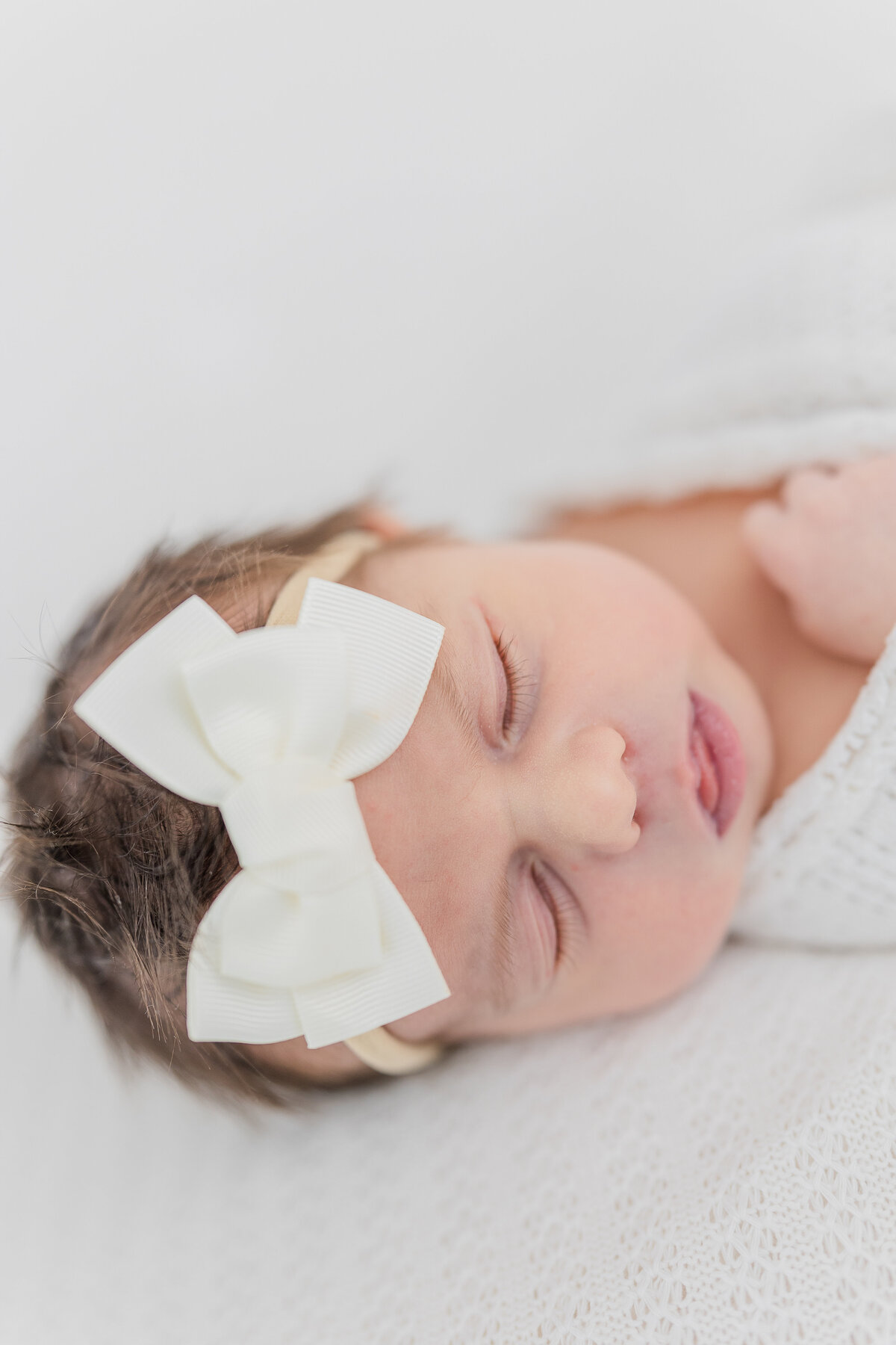 Close up image of newborn baby girl wearing a white bow