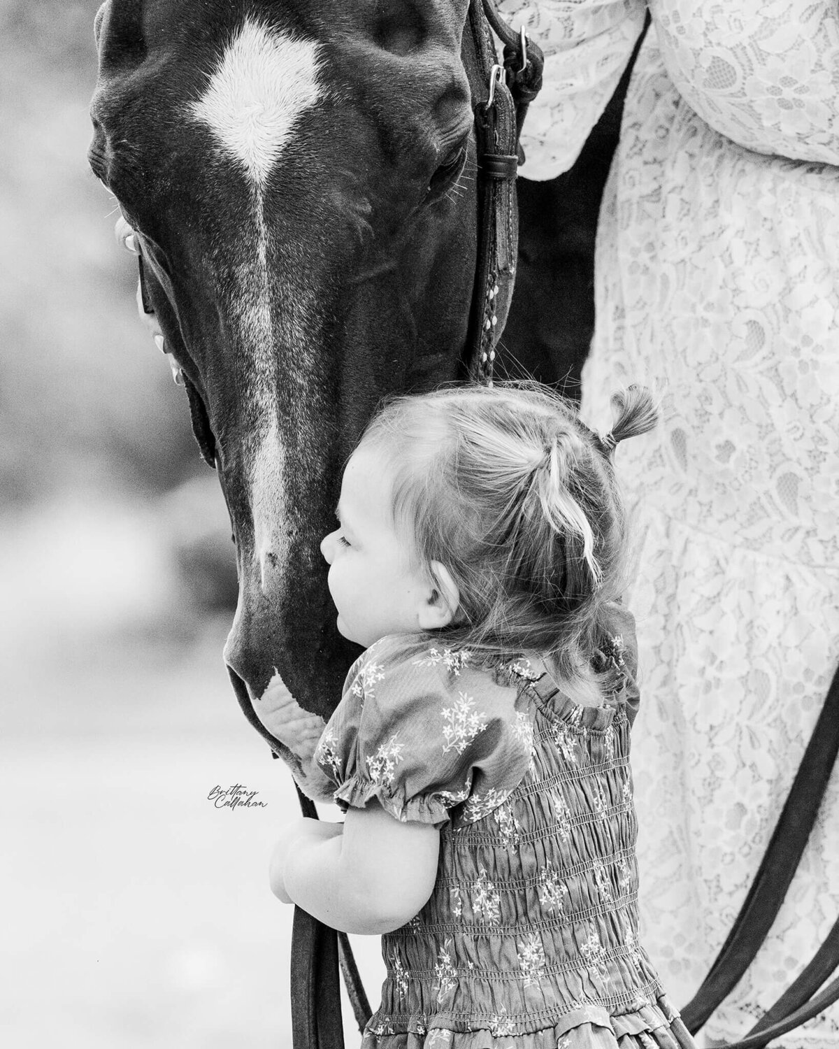 black and white photo of a young girl in pig tails hugging her quarter horse gelding's face  in a sweet moment.