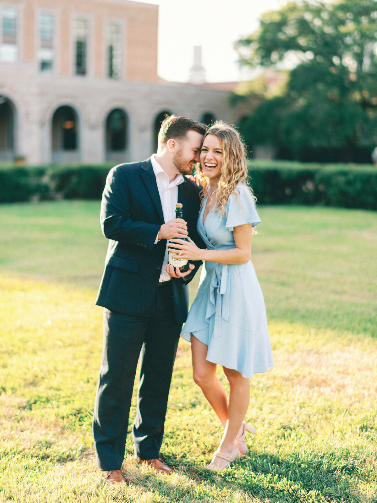bride in blue and groom popping champagne at rice university for engagement photos