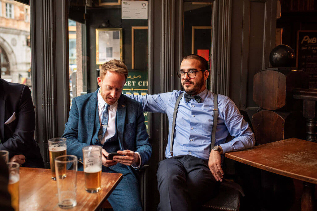 Groom looking at phone with best man in London pub
