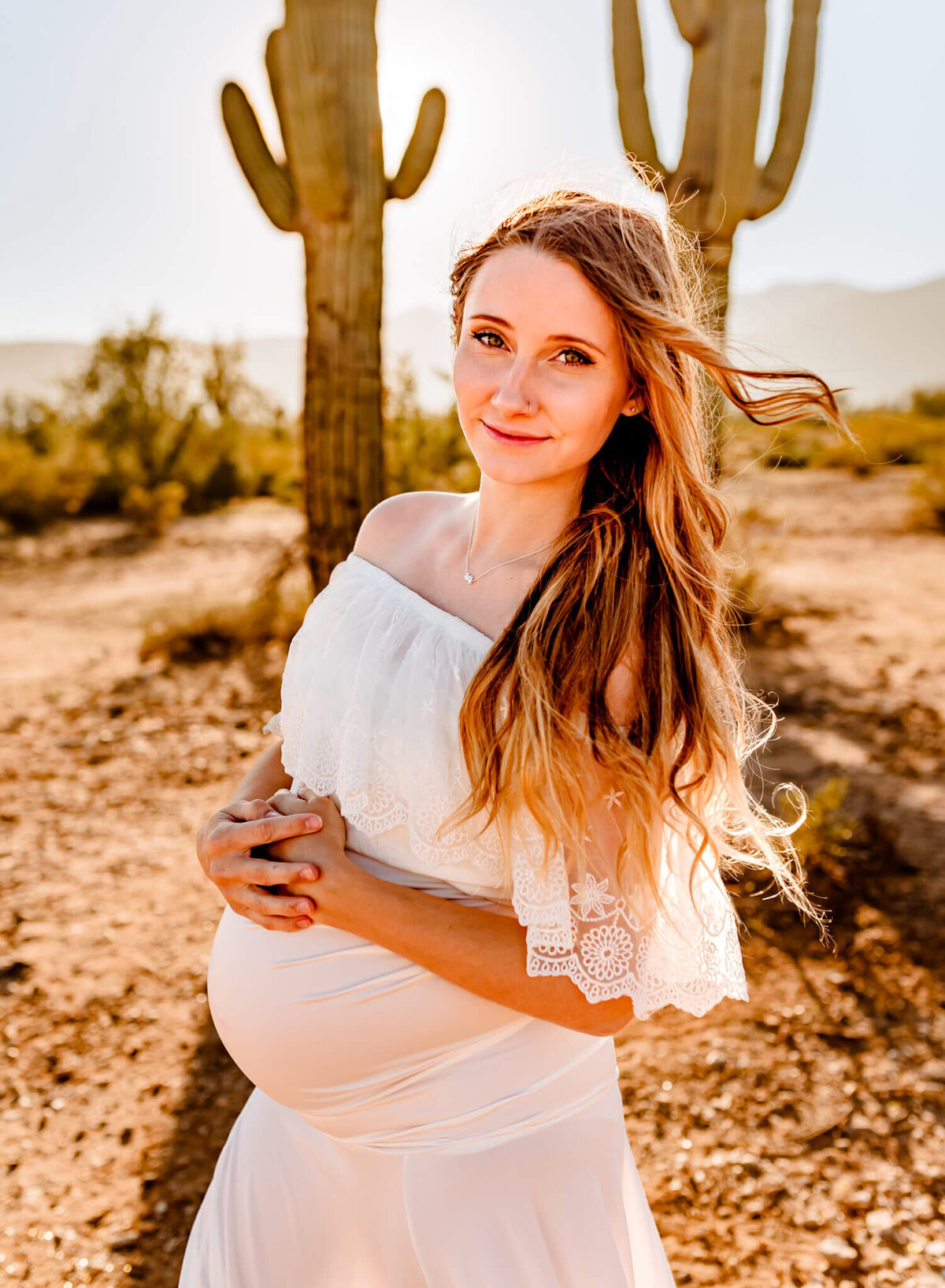 Mom-to-be smiling in Arizona desert while holding her belly for photography