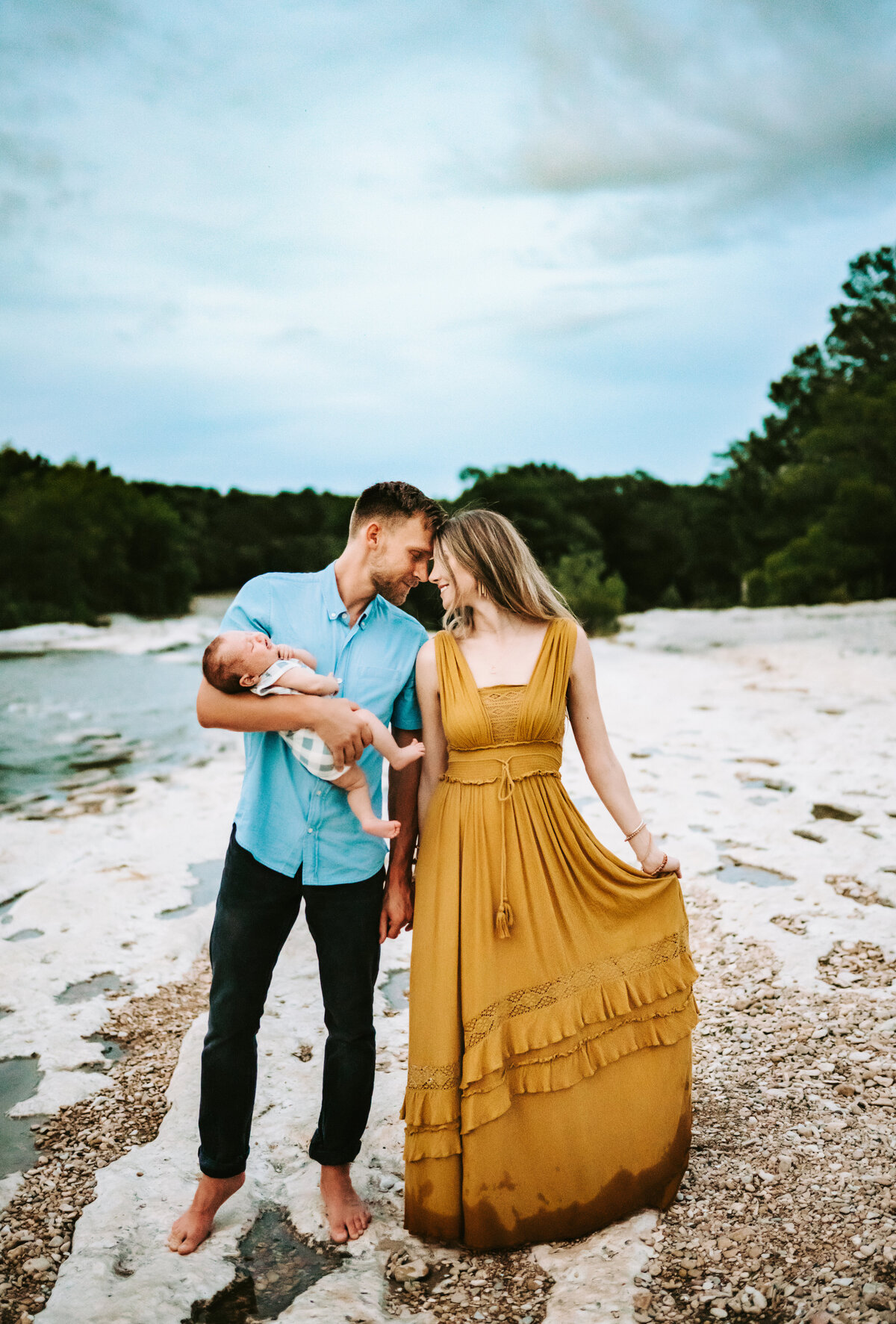 Family Photographer, husband and wife walk on a beach with their newborn child