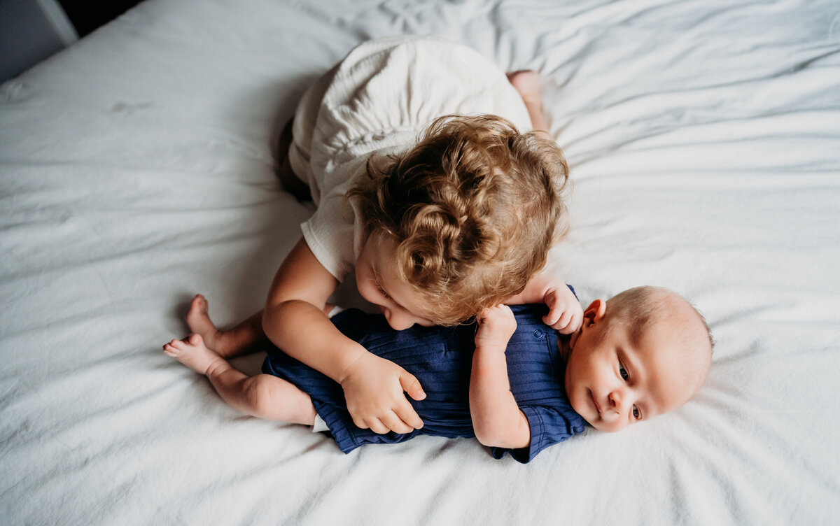 Newborn Photographer, an older sister hugs her new baby brother on the bed