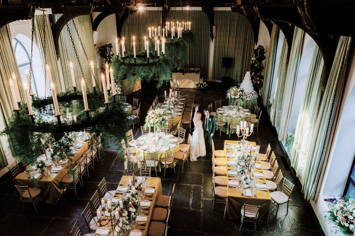 Top view of an elegant room with chandeliers, bronze tables and chairs with large flower bouquet and candle centerpieces