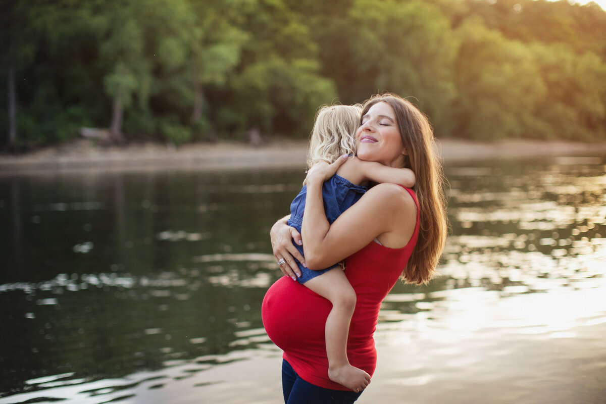 pregnant mom and little girl hugging with river in the background