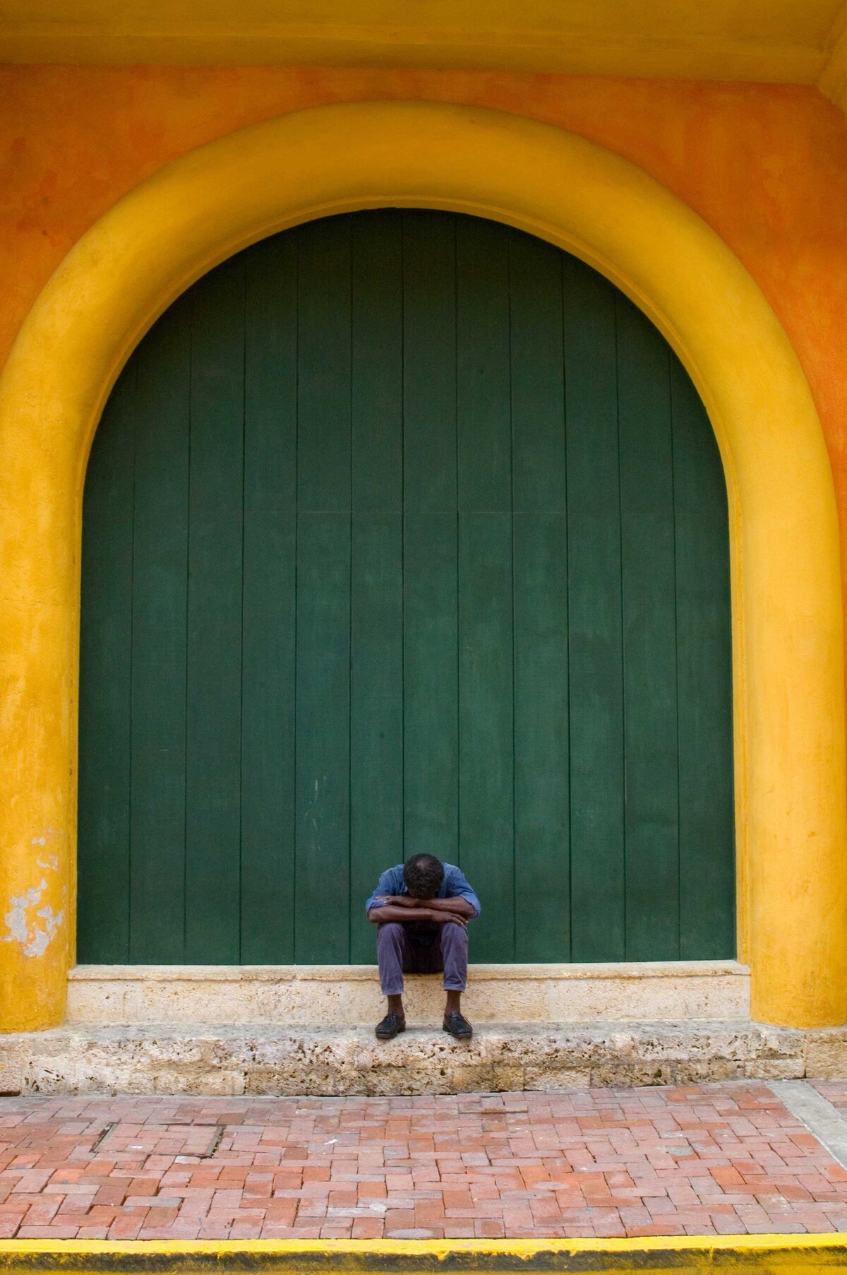 A man sits in front of green door near orange and yellow building in Cartagena Columbia