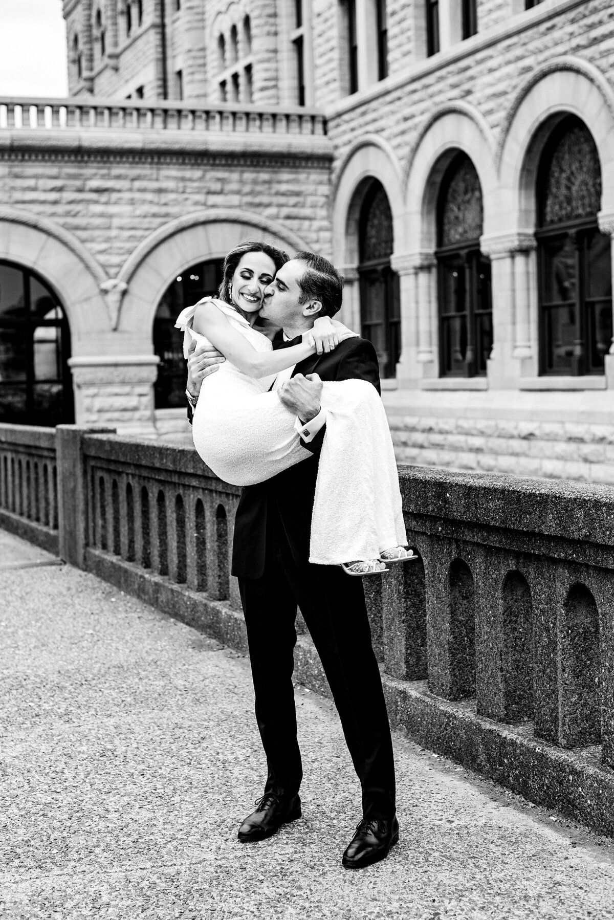 Black and white photo of groom lifting his wife and kissing her on the check in front of Union Station Nashville