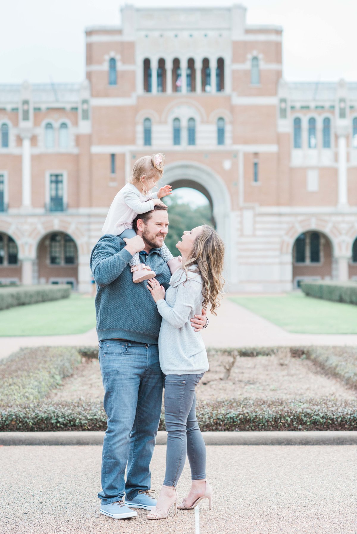 toddler girl on dad's shoulder and mom laughing on Rice University campus