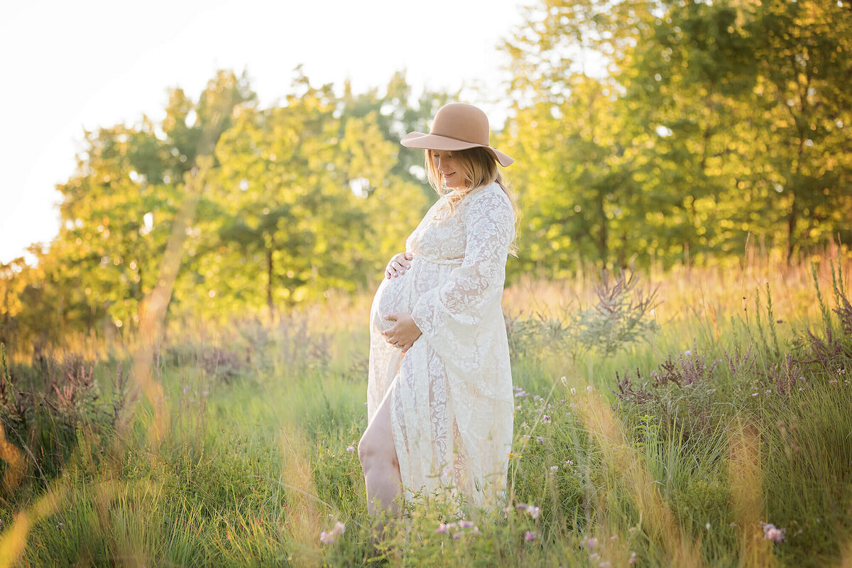 Expectant mother wearing a white gown and a large straw hat during her maternity photoshoot.