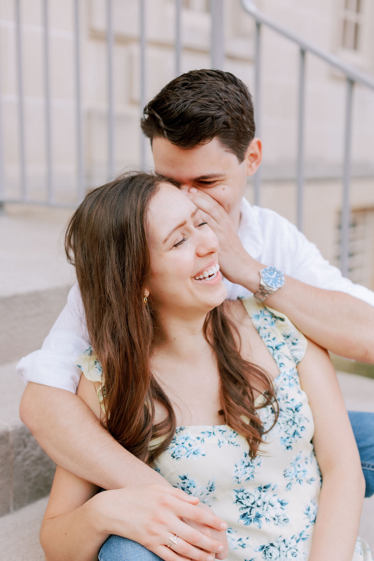 Engagement photo of man whispering into woman's ear