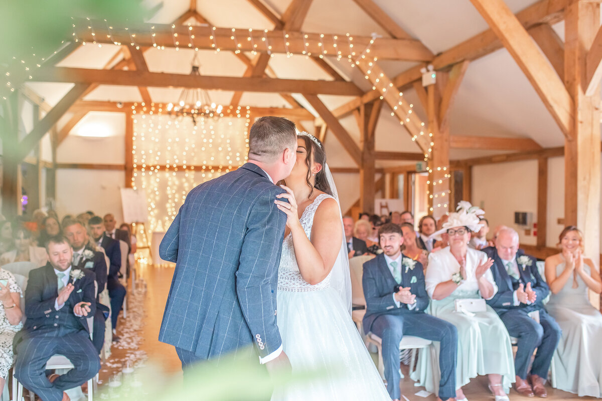 Bride and groom sharing their first kiss in Sandhole Oak Barn ceremony room