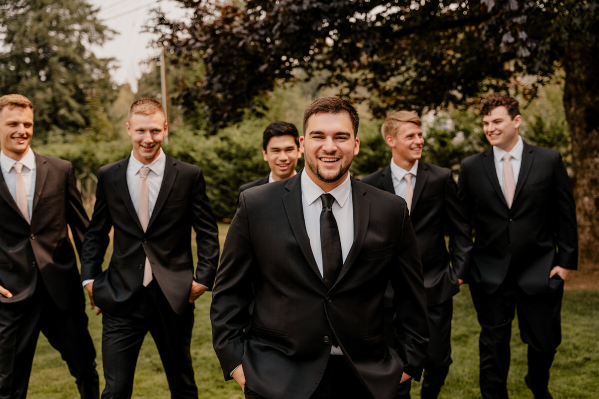The groom and groomsmen all walk, smiling, toward the camera in their classy black suits.