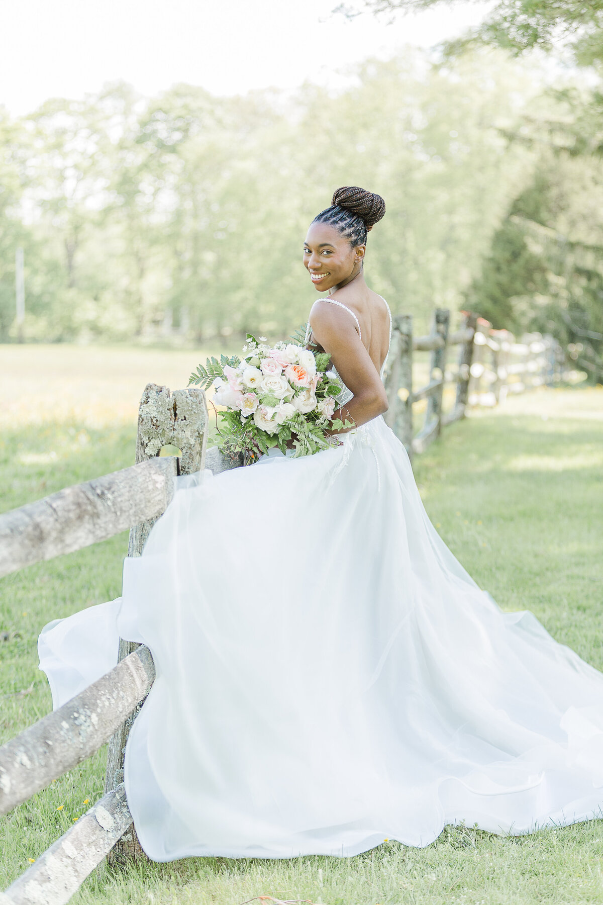Bride poses alongside a wooden fence Her back is to the camera and she is looking over her shoulder and smiling. Captured by RI Wedding Photographer Lia Rose Weddings