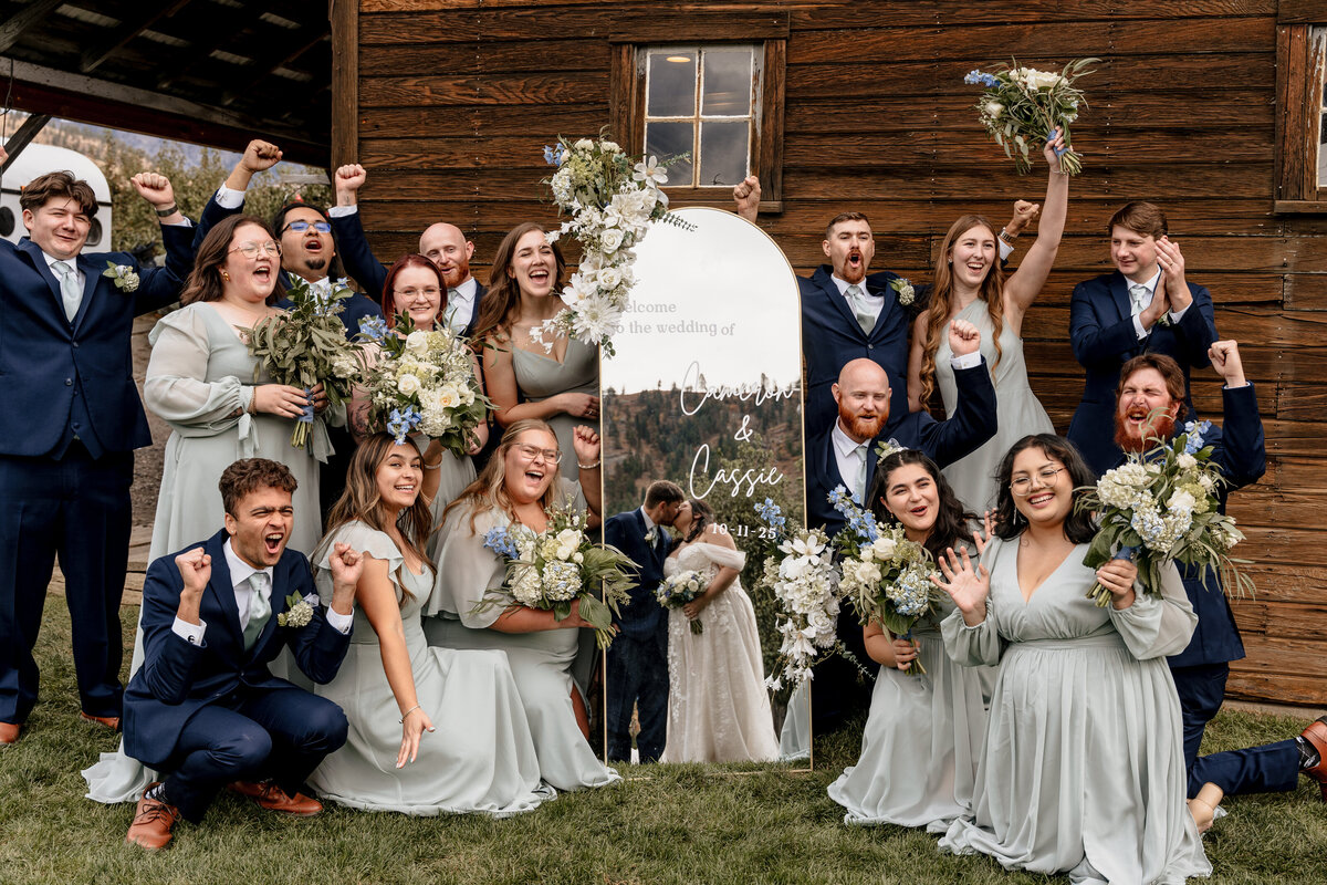 The wedding cheers while standing by a long mirror, which reflects the bride and groom kissing.
