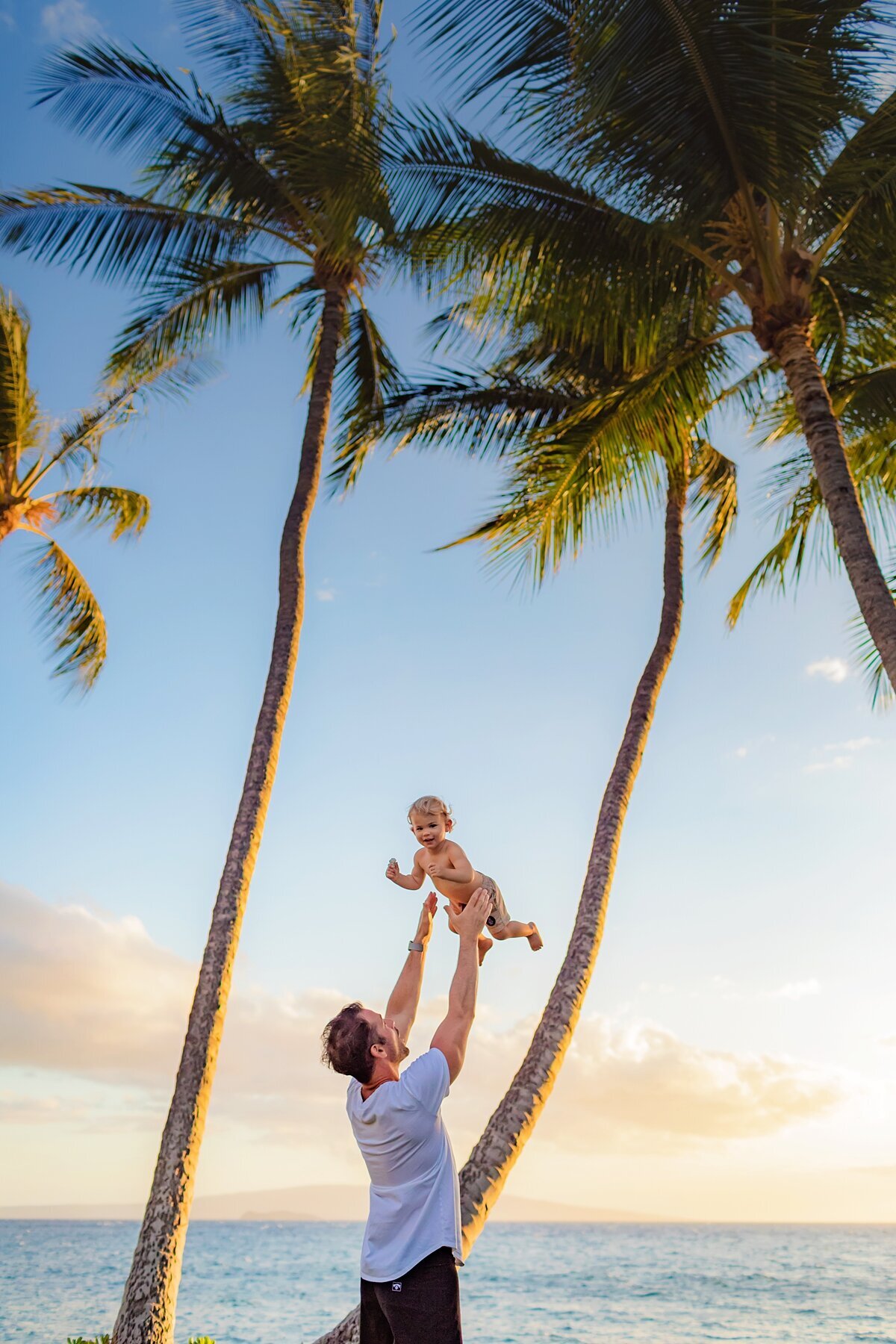 Dad lifts his child underneath palm tress in Wailea during his photo shoot with Love + Water