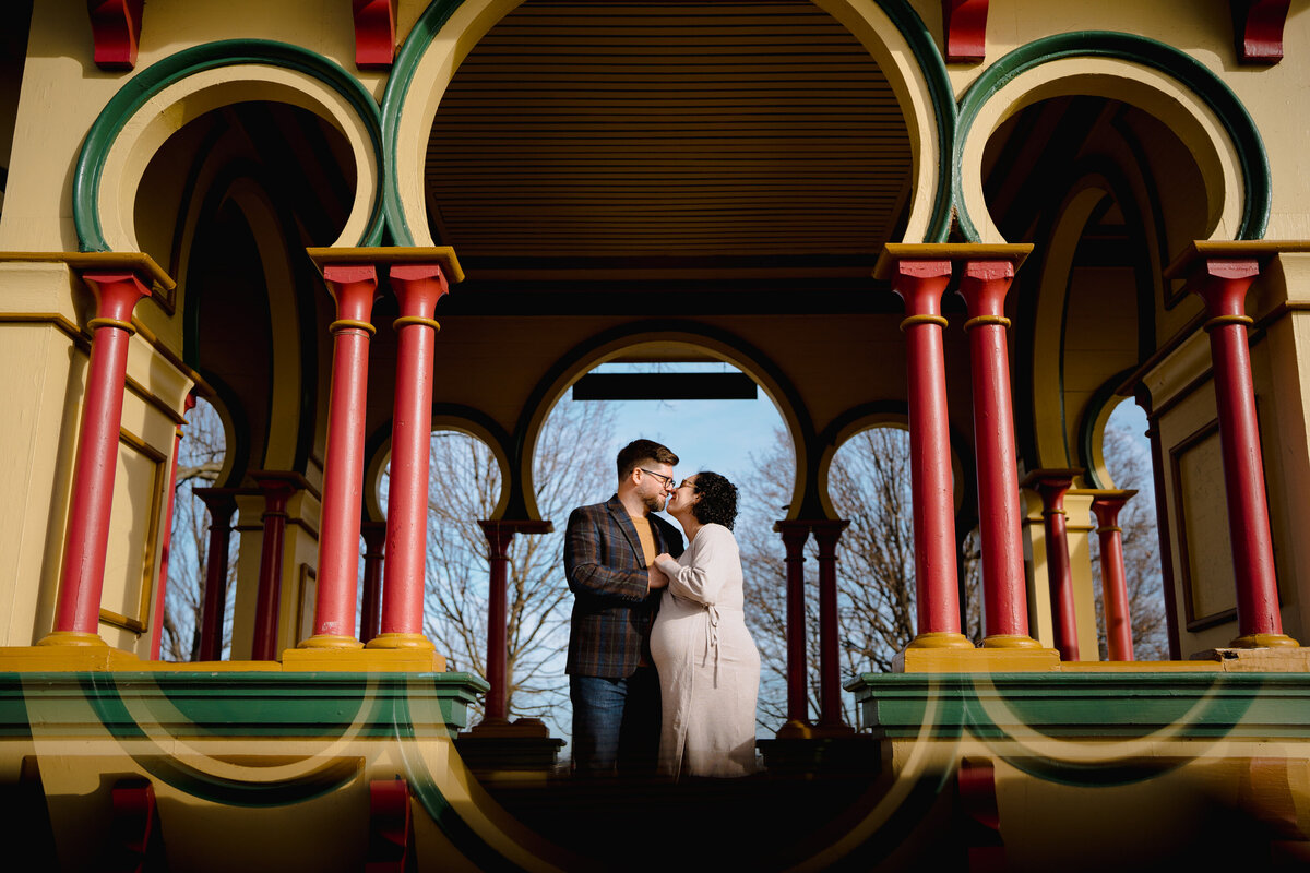 A pregnant person about to kiss their partner under a colorful gazebo.