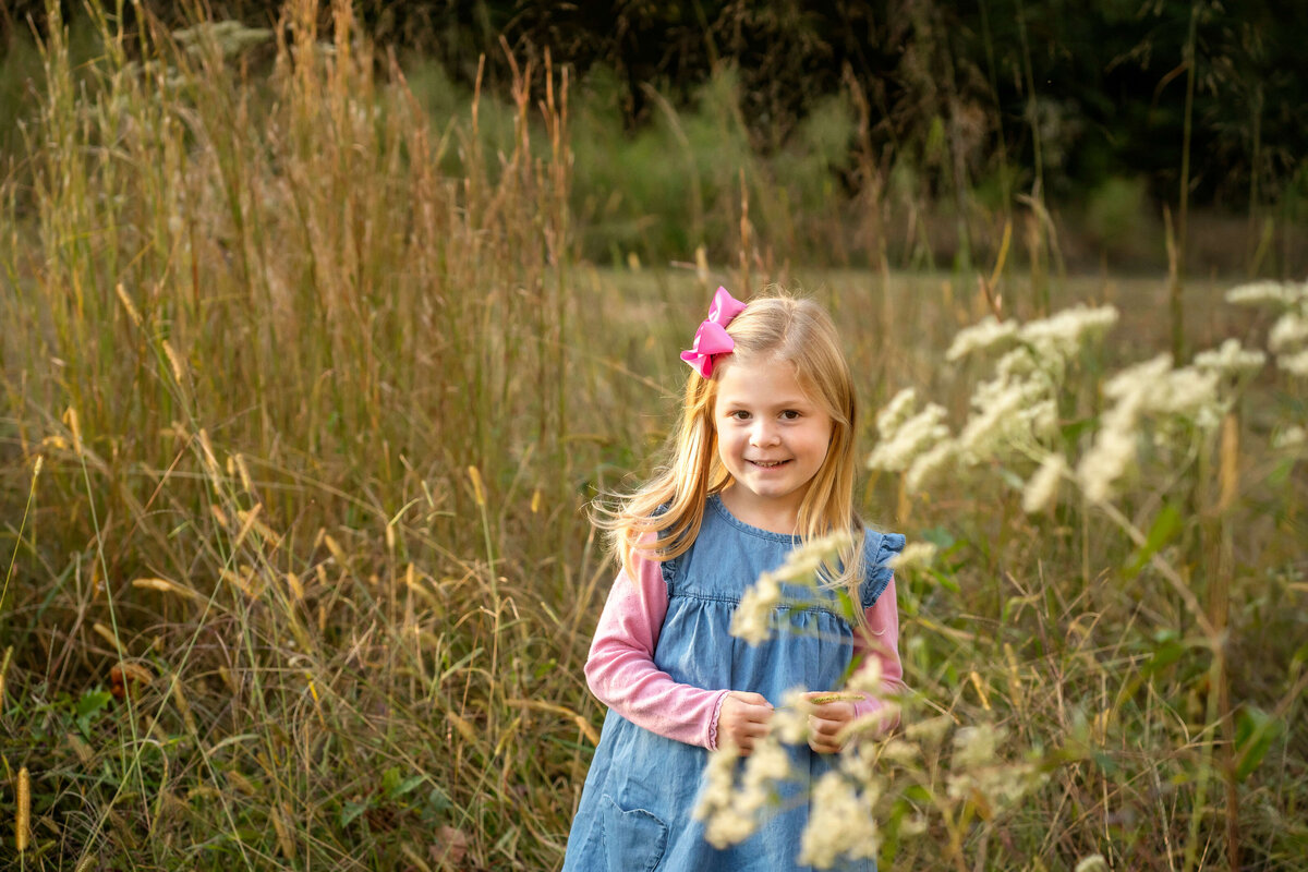5 year old girl smiling at the camera in a field of tall grass and flowers.