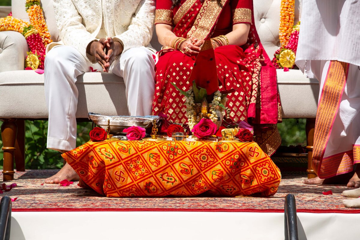 A close-up view of a bride and groom sitting side by side in traditional Indian attire during an Iowa wedding ceremony, with ornate floral decorations and fabrics visible.