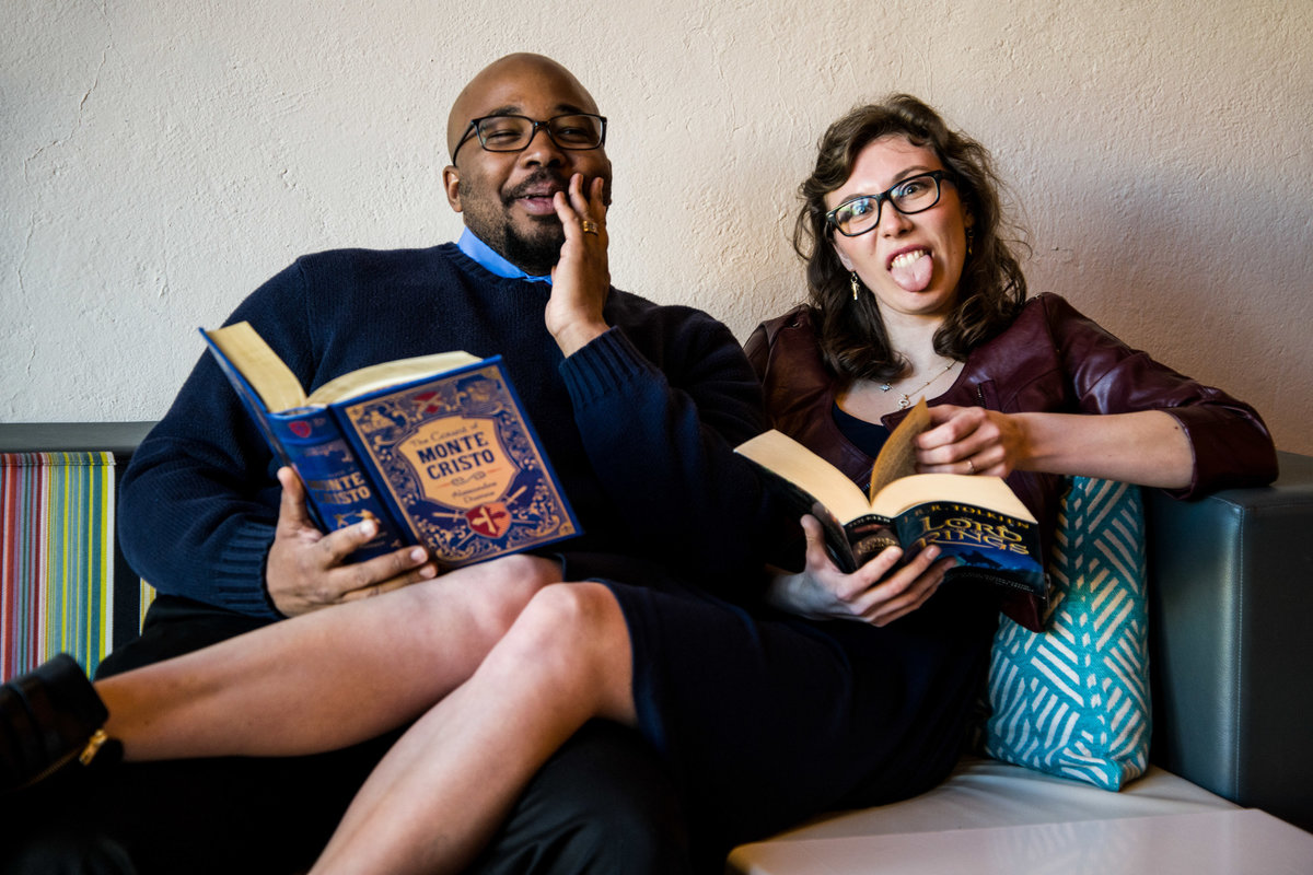 Black man and woman with glasses laugh while holding books.