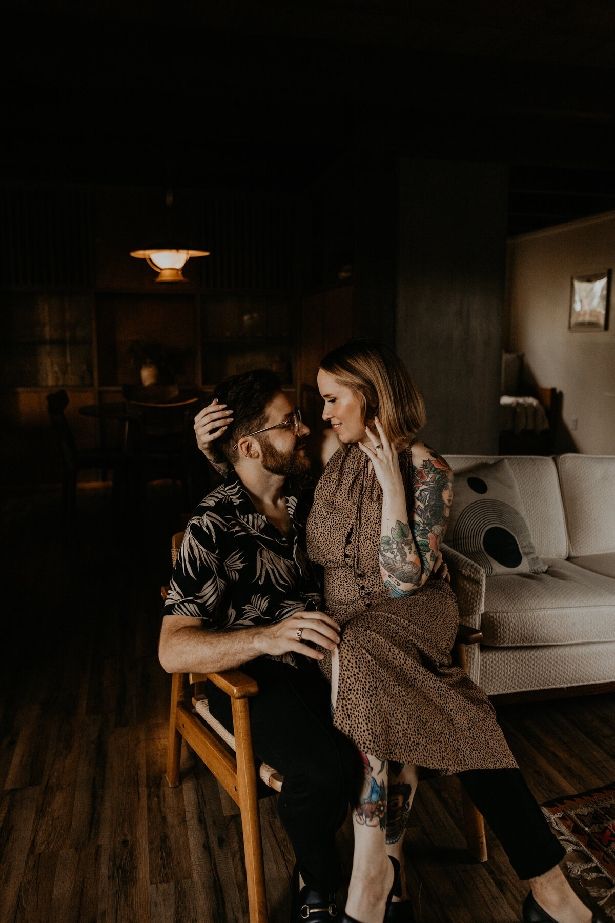 engaged couple sitting on a couch together in a midcentury living room