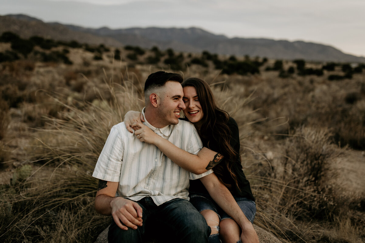 engaged couple sitting and hugging in the desert