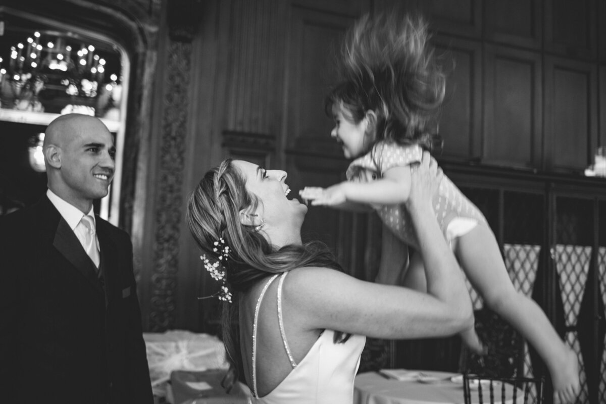 A bride lifting up a small child and smiling.