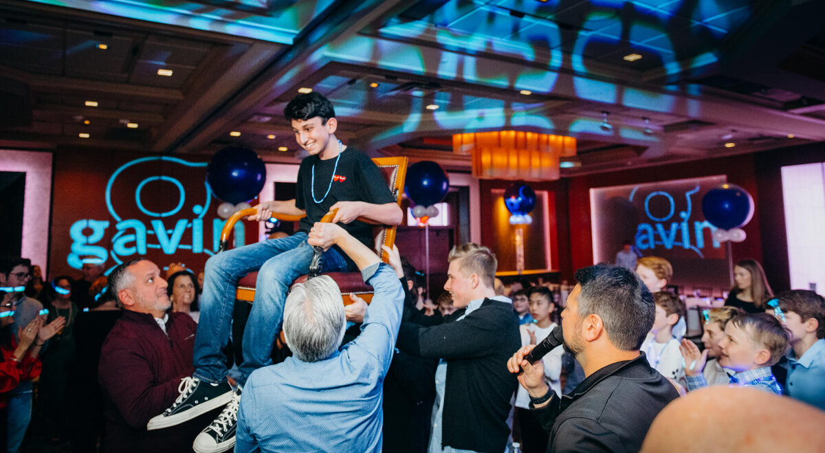 An image of Bellevue Bar and Bat Mitzvah Photography with a boy being lifted in a chair on a crowded dance floor