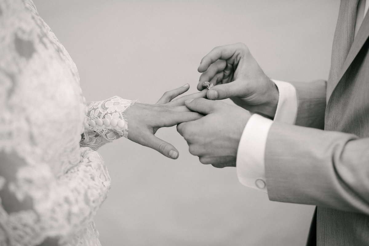 Close up of groom placing wedding ring on  bride's ring finger, in black and white